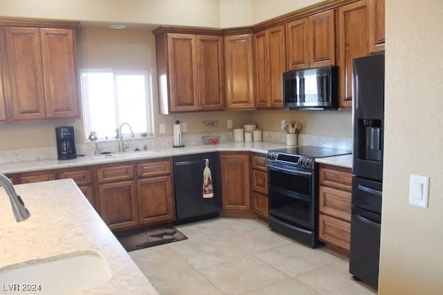 kitchen featuring sink, light tile patterned floors, light stone counters, and black appliances