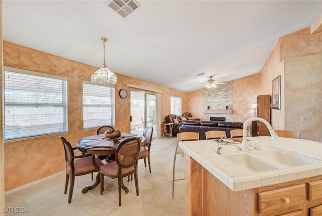 kitchen featuring a large fireplace, ceiling fan with notable chandelier, tile countertops, sink, and a kitchen island