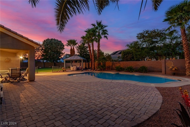 pool at dusk featuring a gazebo and a patio area