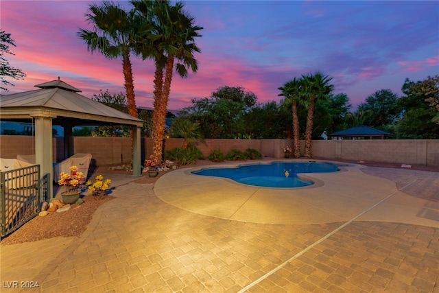 pool at dusk with a gazebo and a patio area