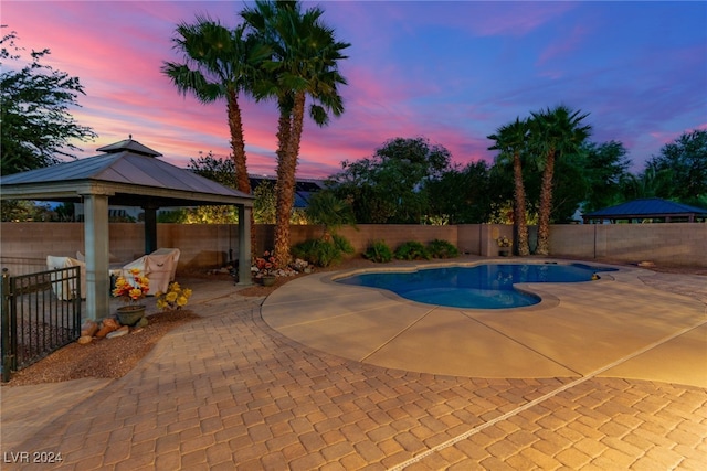 pool at dusk featuring a gazebo and a patio