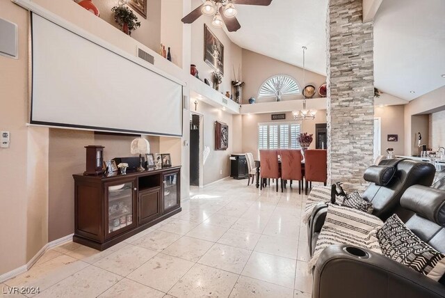 living room with visible vents, high vaulted ceiling, ceiling fan with notable chandelier, light tile patterned floors, and decorative columns