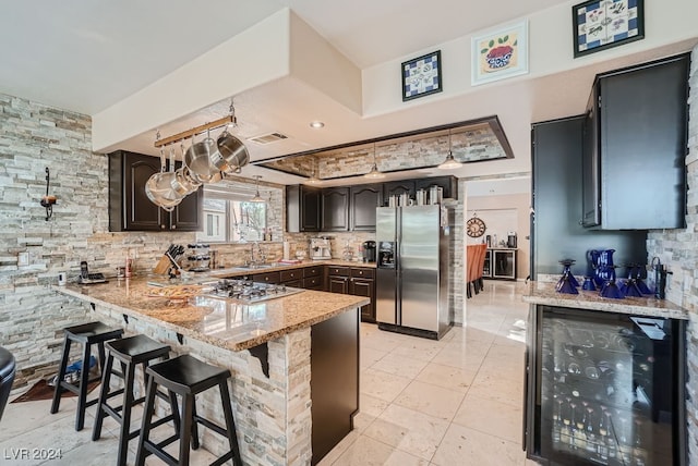 kitchen with light stone counters, stainless steel appliances, kitchen peninsula, beverage cooler, and a kitchen bar