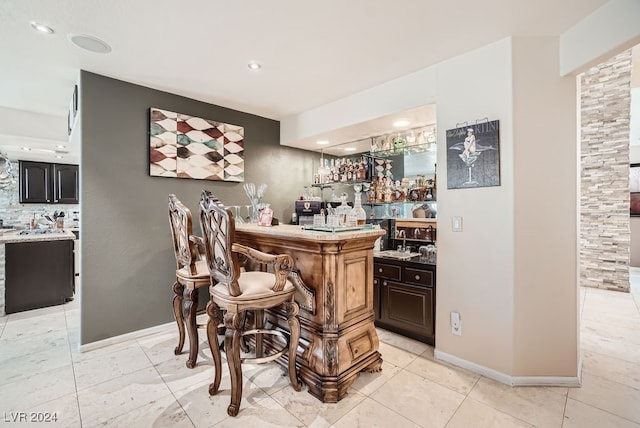 bar with light tile patterned floors, tasteful backsplash, sink, and stone counters