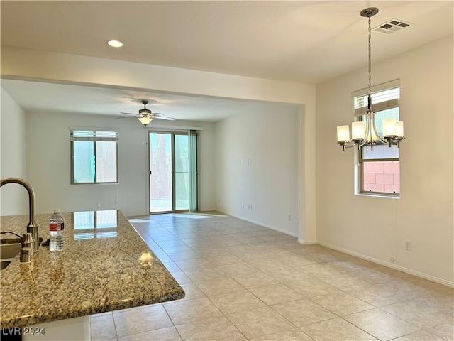 interior space with light tile patterned floors, stone counters, ceiling fan with notable chandelier, sink, and pendant lighting