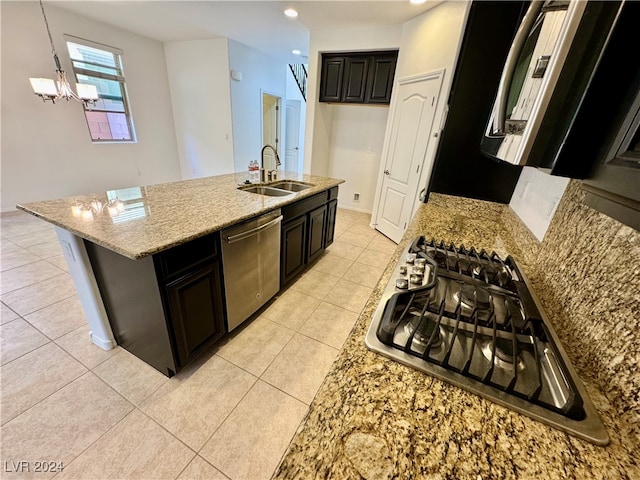 kitchen featuring decorative light fixtures, stainless steel appliances, sink, light stone countertops, and a center island with sink