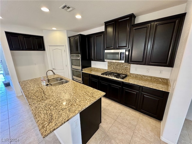 kitchen with light stone counters, sink, appliances with stainless steel finishes, and a kitchen island with sink