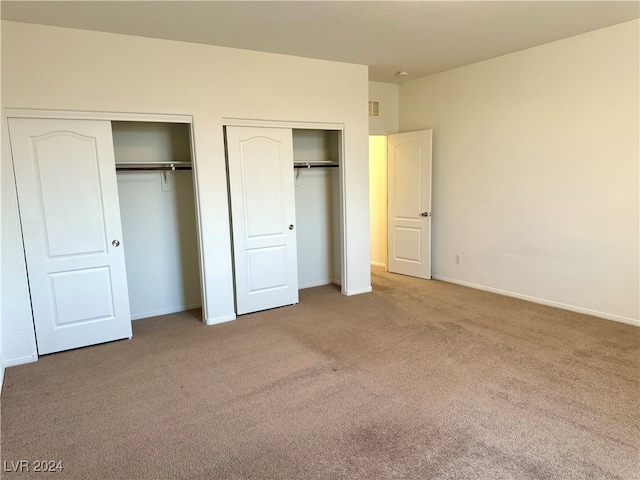 unfurnished bedroom featuring multiple closets and light colored carpet