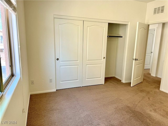 unfurnished bedroom with light colored carpet and a closet