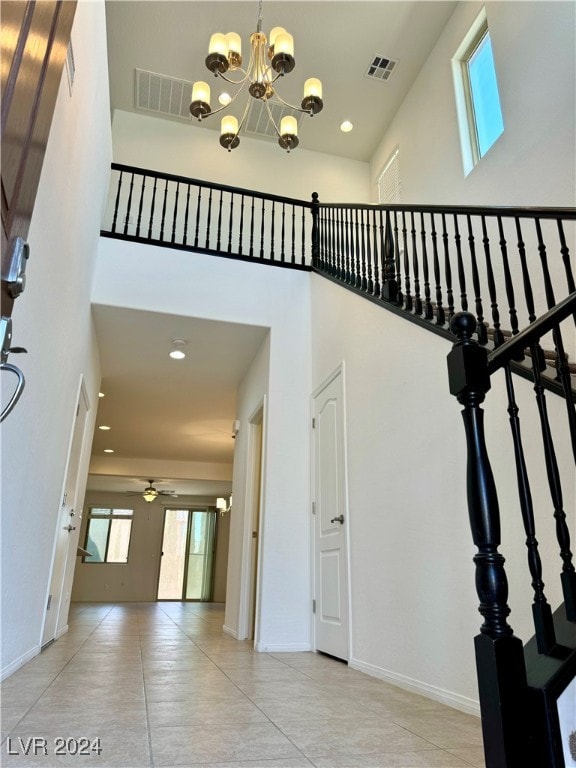 stairs with tile patterned flooring, a towering ceiling, and ceiling fan with notable chandelier