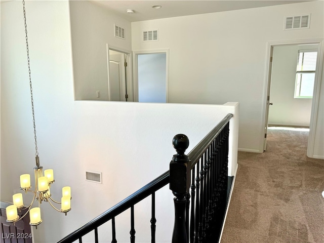 hallway with light colored carpet and a chandelier