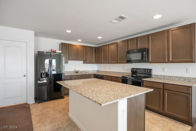 kitchen featuring black appliances, a kitchen island, light stone counters, and dark brown cabinets