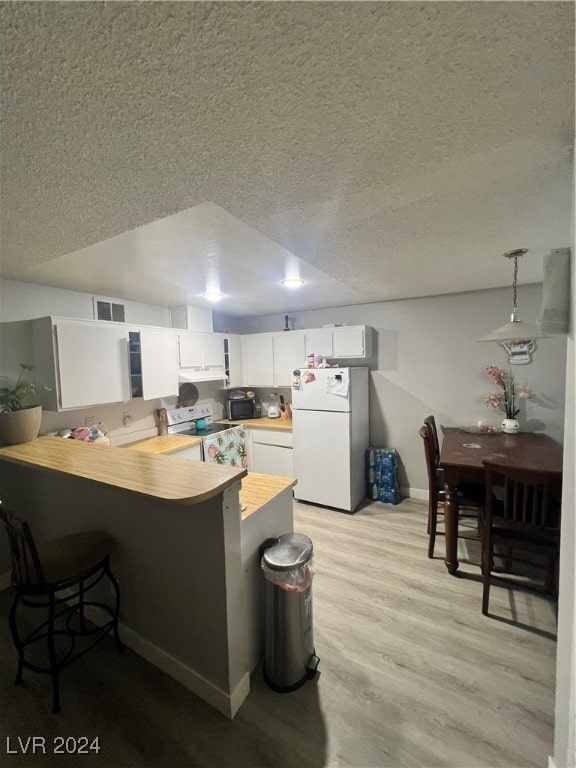 kitchen featuring kitchen peninsula, decorative light fixtures, light wood-type flooring, white cabinets, and white appliances