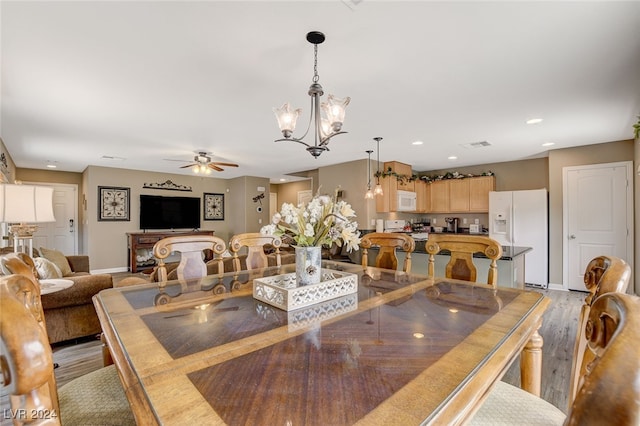 dining space with ceiling fan with notable chandelier and light hardwood / wood-style floors