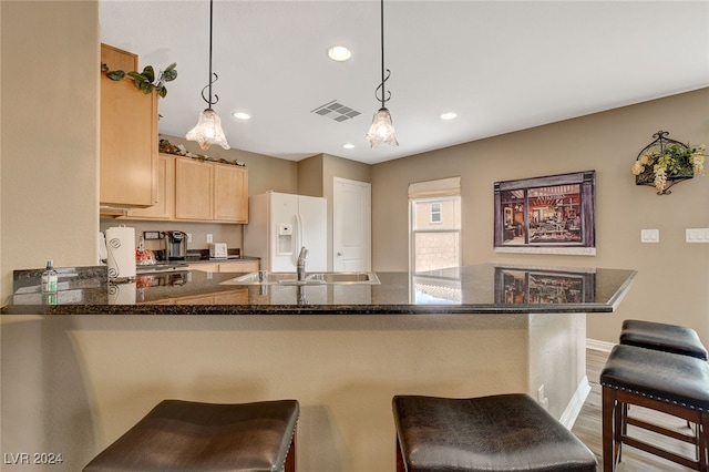 kitchen featuring hanging light fixtures, sink, light brown cabinets, kitchen peninsula, and a breakfast bar area