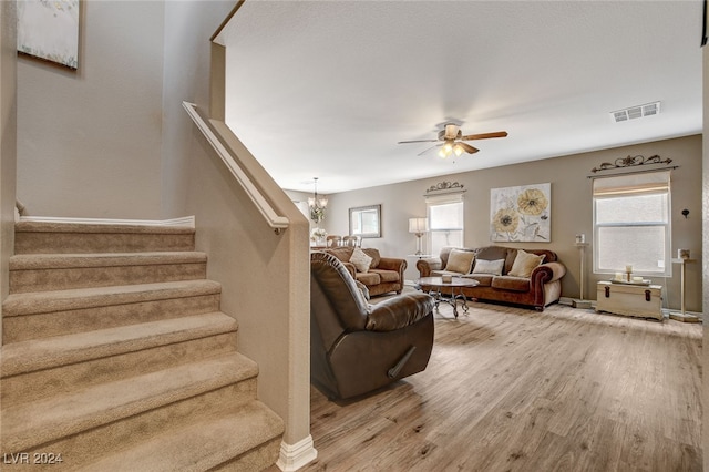 living room with ceiling fan with notable chandelier and light hardwood / wood-style flooring