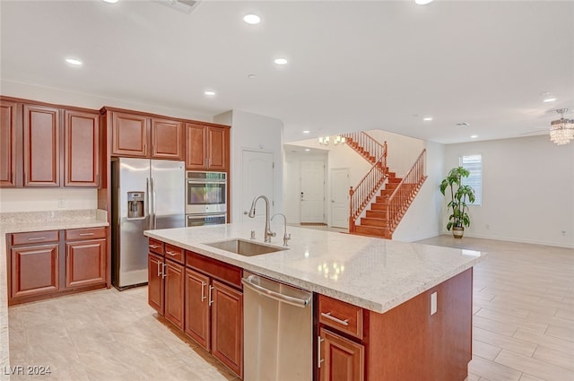 kitchen with light hardwood / wood-style floors, light stone countertops, stainless steel appliances, a center island with sink, and sink