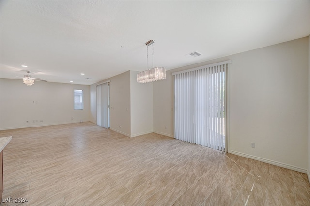 empty room featuring ceiling fan with notable chandelier and light hardwood / wood-style floors