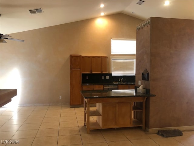 kitchen featuring kitchen peninsula, dark stone counters, ceiling fan, light tile patterned floors, and high vaulted ceiling