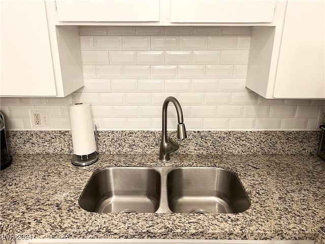 interior details with decorative backsplash, white cabinets, dark stone counters, and sink