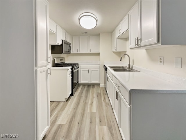 kitchen with stainless steel appliances, sink, white cabinetry, and light hardwood / wood-style floors