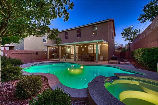 pool at dusk with a patio area and an in ground hot tub