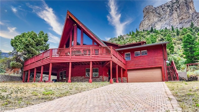 log home featuring stairway, a wooden deck, decorative driveway, stone siding, and a garage