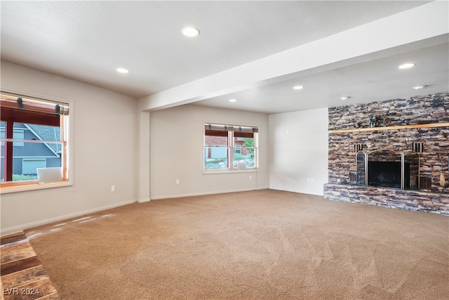 unfurnished living room featuring carpet floors, beam ceiling, and a stone fireplace