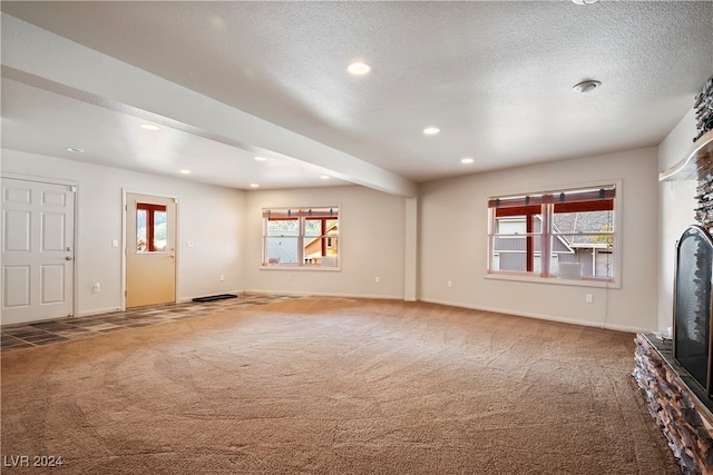 unfurnished living room with carpet flooring, a textured ceiling, and a stone fireplace