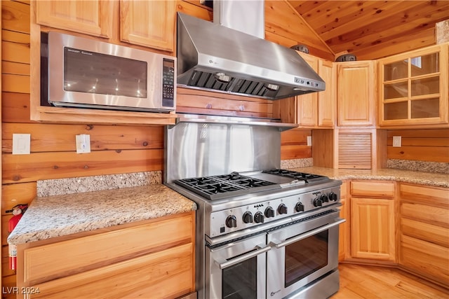 kitchen with wooden walls, vaulted ceiling, light wood-type flooring, stainless steel appliances, and exhaust hood