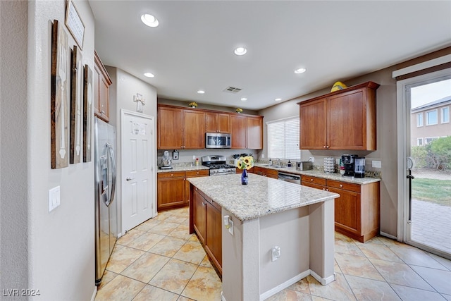 kitchen featuring appliances with stainless steel finishes, a wealth of natural light, light stone counters, and a center island