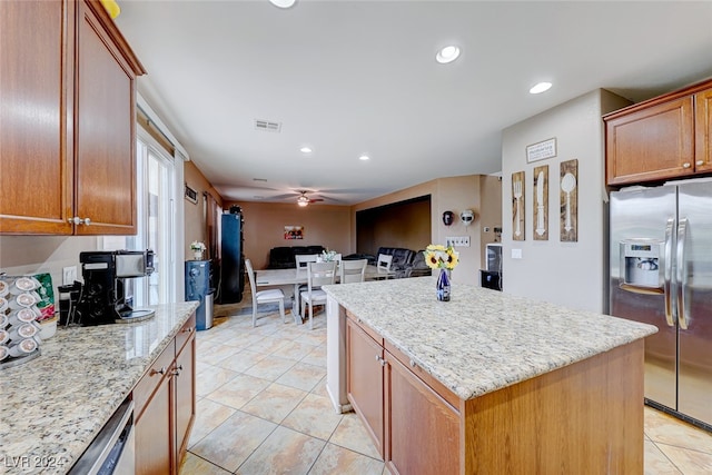 kitchen featuring light tile patterned floors, light stone counters, stainless steel refrigerator with ice dispenser, ceiling fan, and a kitchen island