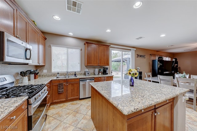 kitchen with appliances with stainless steel finishes, light stone counters, a center island, and sink