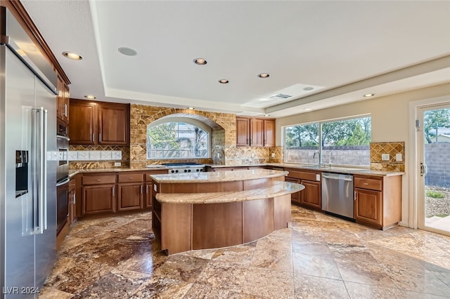 kitchen featuring a raised ceiling, appliances with stainless steel finishes, decorative backsplash, a kitchen island, and sink