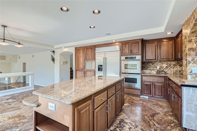 kitchen with light stone counters, hanging light fixtures, stainless steel appliances, decorative backsplash, and a kitchen island