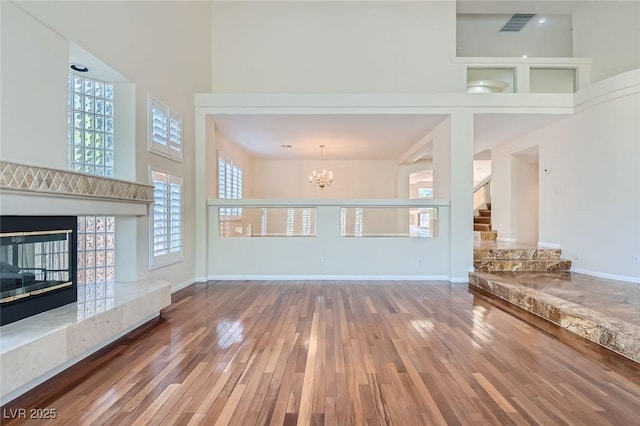 unfurnished living room featuring a high ceiling, a high end fireplace, a chandelier, and wood-type flooring