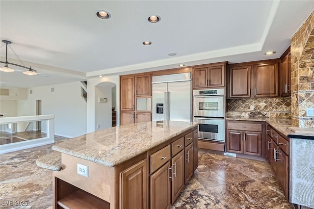 kitchen featuring a center island, light stone counters, decorative backsplash, pendant lighting, and appliances with stainless steel finishes