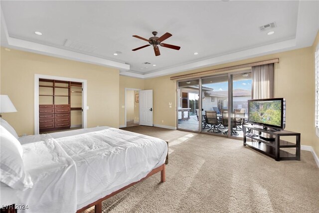 bedroom with light colored carpet, a tray ceiling, a spacious closet, access to outside, and ceiling fan