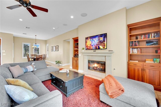 living room with built in features, ceiling fan, and a tiled fireplace