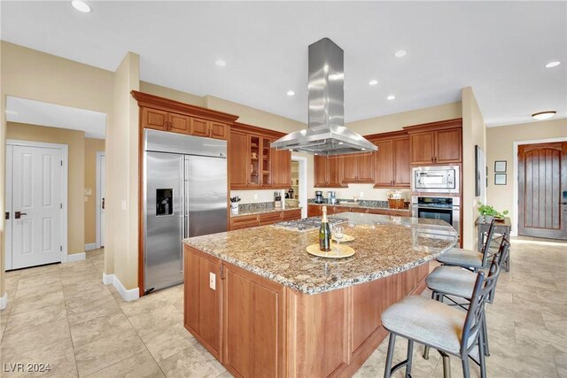 kitchen featuring built in appliances, a kitchen breakfast bar, a kitchen island, light stone counters, and island exhaust hood