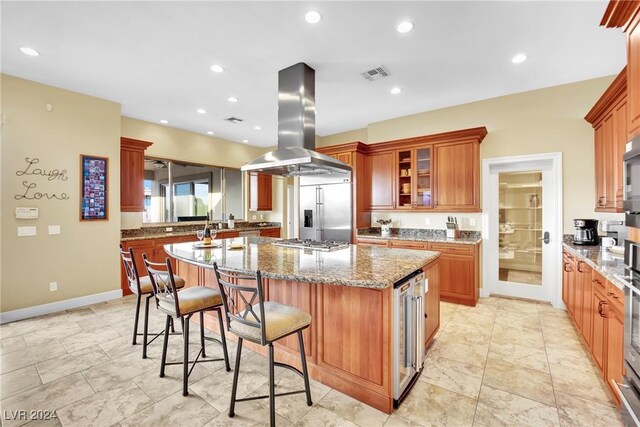 kitchen with stone counters, wine cooler, a center island, a breakfast bar, and island exhaust hood