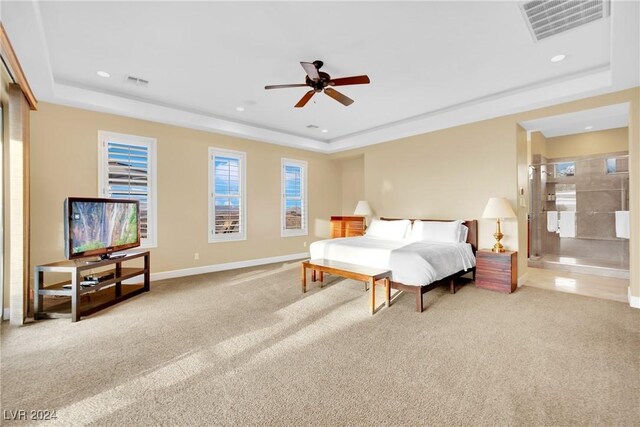 bedroom with ensuite bath, a raised ceiling, ceiling fan, and light colored carpet