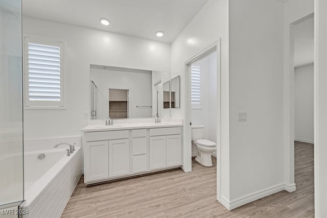 bathroom with hardwood / wood-style floors, toilet, a relaxing tiled tub, and vanity