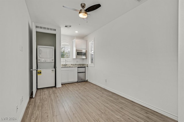 unfurnished bedroom featuring stacked washing maching and dryer, light hardwood / wood-style floors, stainless steel refrigerator, sink, and ceiling fan