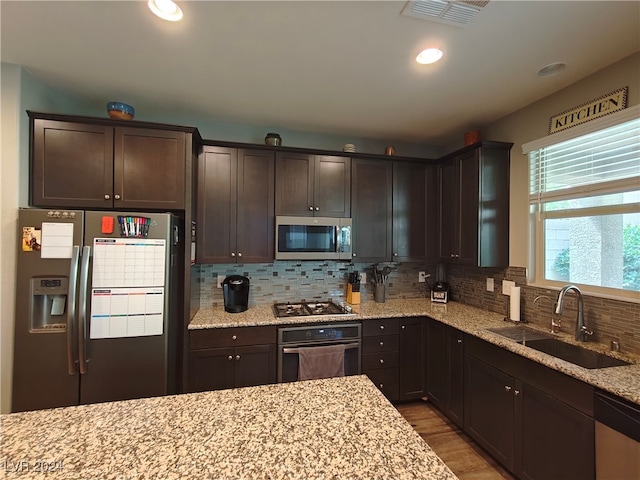 kitchen with dark brown cabinets, light hardwood / wood-style flooring, light stone counters, sink, and appliances with stainless steel finishes