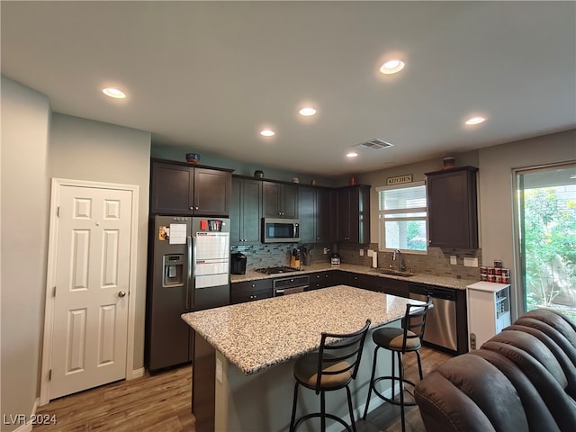 kitchen featuring dark brown cabinets, a kitchen bar, wood-type flooring, a center island, and appliances with stainless steel finishes