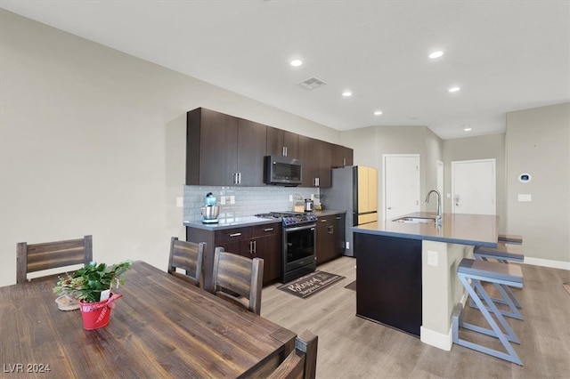 kitchen featuring light hardwood / wood-style flooring, appliances with stainless steel finishes, dark brown cabinets, and a kitchen island with sink