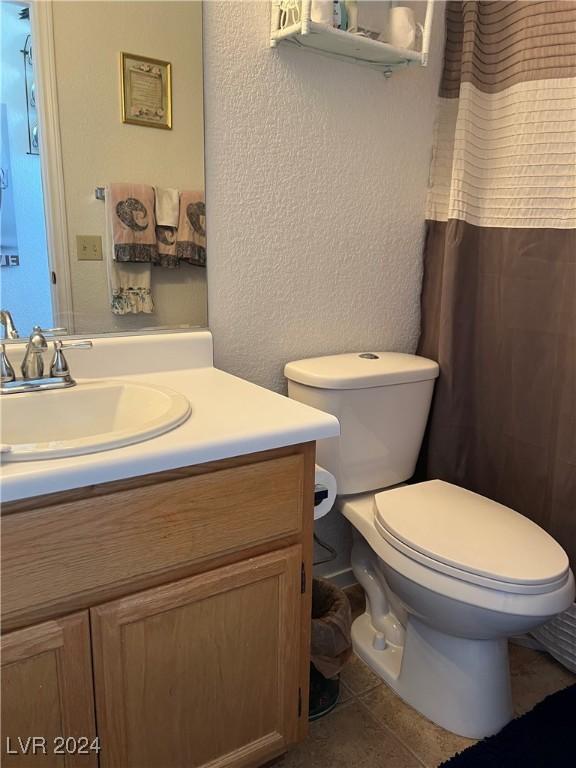 bathroom with a textured wall, vanity, toilet, and tile patterned floors