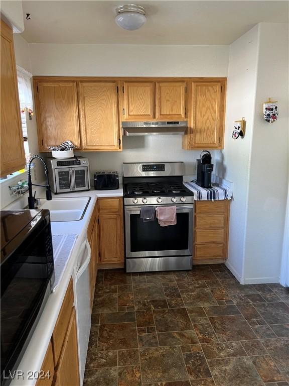 kitchen with stone finish floor, stainless steel gas range, white dishwasher, under cabinet range hood, and a sink