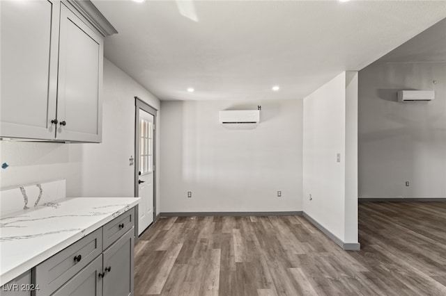 interior space with gray cabinets, light stone countertops, wood-type flooring, and a wall unit AC